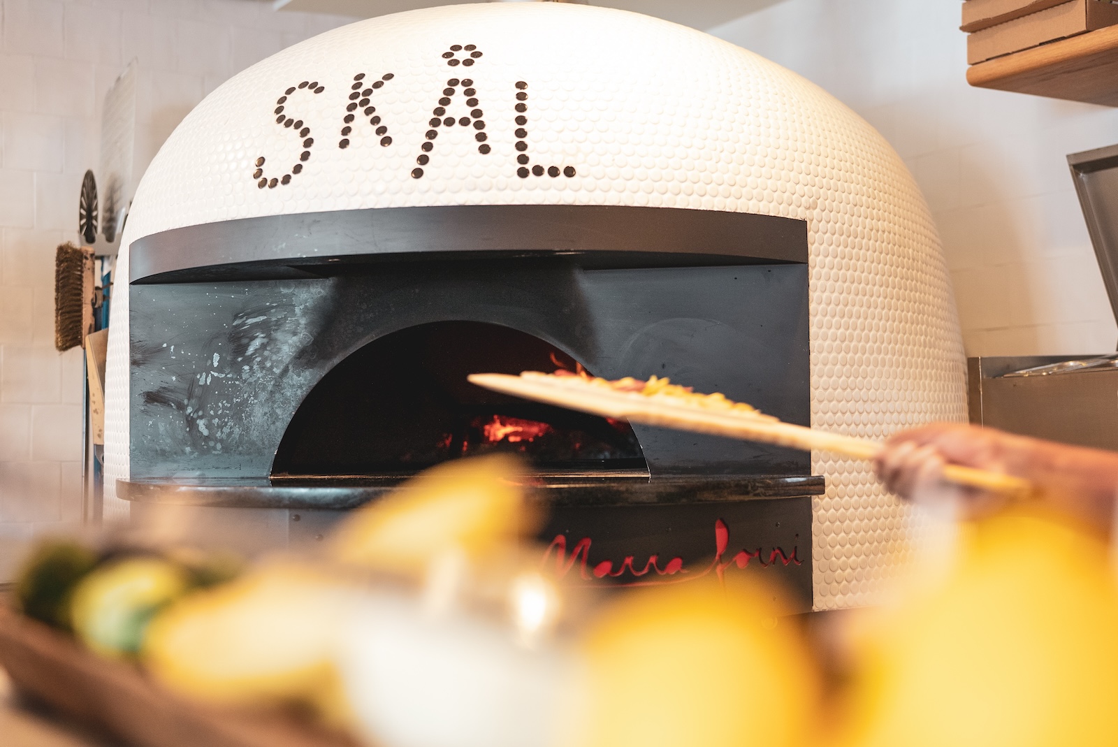 A pizza on a wooden board being put into our Wood-Fired pizza oven.